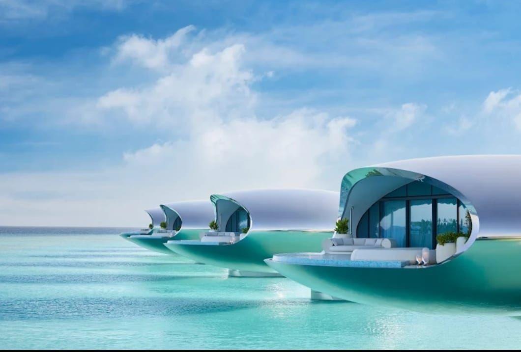 Futuristic floating villas with curved roofs on turquoise water under a blue sky.