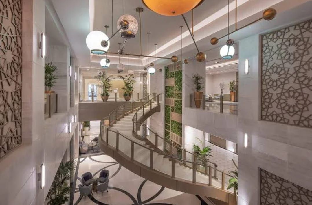 Elegant hotel lobby with spiral staircase, modern lighting, and decorative walls with plants.