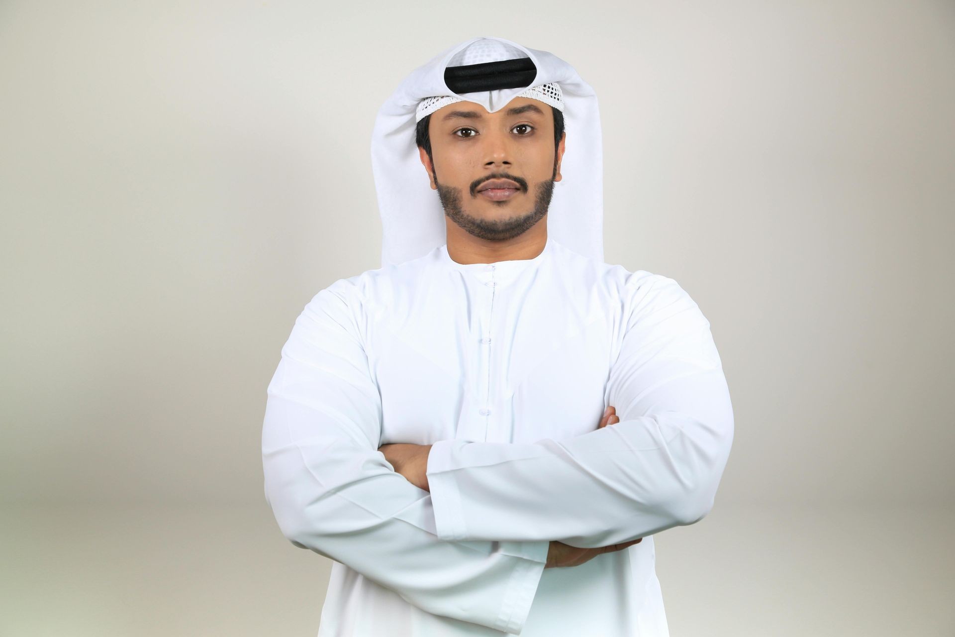 Person wearing traditional white Middle Eastern attire with arms crossed against a neutral background.